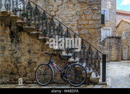 Budva, Montenegro - Mai 30, 2019: Bike lehnte sich gegen eine alte Mauer aus Stein auf einer Straße von der gut erhaltenen mittelalterlichen Altstadt auf dem Balkan Stockfoto