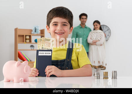 Junge zeigt Bankbuch und seine Eltern im Hintergrund Stockfoto