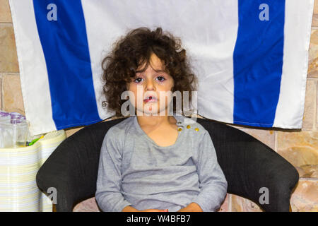 5. Mai 2018 ein hübsches junges jüdisches Mädchen sitzt ruhig vor einem israelischen Flagge als ihre Eltern an Kunden in Ihrem Restaurant in Nazaret besuchen Stockfoto