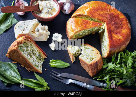 Close-up von Spinat grüne Bohne und Blue Cheese pie in Scheiben geschnitten auf schwarzem Schiefer Fach mit blauen Käse Sahne in einer Schüssel auf einer konkreten Tabelle, horizontal Stockfoto