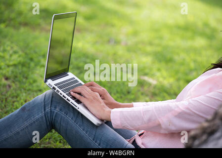 Junge schöne Frau im Freien in einem öffentlichen Park. Arbeiten am Laptop im Freien. Zugeschnittenes Bild der weiblichen Arbeiten am Laptop während der Sitzung in einem Park. Stockfoto