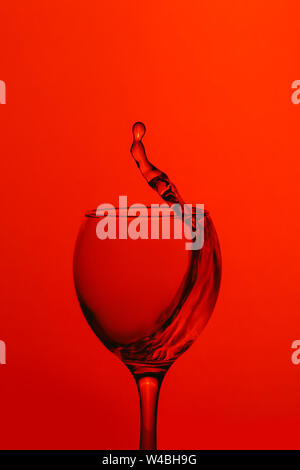 Wasser im Weinglas auf rotem Hintergrund isoliert. Stockfoto