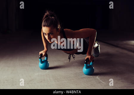 Athlet Frau tun Push-ups auf zwei Kettlebells Stockfoto