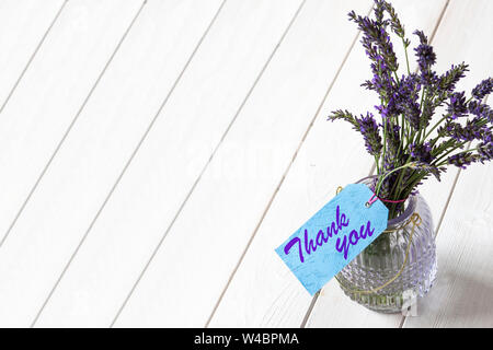 Bündel von Lavendel in einem Glas Laterne Glas, mit vielen Dank, dass Sie sich auf einem blauen Geschenk Label geschrieben. Weiß Holz Hintergrund Stockfoto