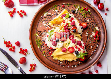 Hausgemachte Pfannkuchen mit saurer Sahne und Beeren auf einem weißen Hintergrund close-up, horizontale Foto, Ansicht von oben Stockfoto