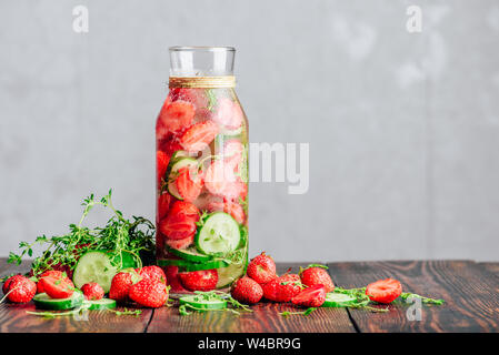 Flasche Wasser hineingegossen mit frischen Erdbeeren, in Scheiben geschnittene Gurken und Federn von Thymian. Zutaten verstreut auf Holztisch. Kopieren Sie Platz. Stockfoto