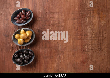 Verschiedene Arten von Oliven in Schalen auf einem dunklen Holzmöbeln im Landhausstil Hintergrund mit kopieren. Lila, Grün mit Mandeln gefüllt, und schwarze Oliven Stockfoto