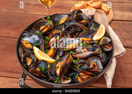 Marinara Muscheln, Moules Mariniere, mit Toastbrot, Zitronenscheiben und Wein auf einem dunklen Holzmöbeln im Landhausstil Hintergrund Stockfoto