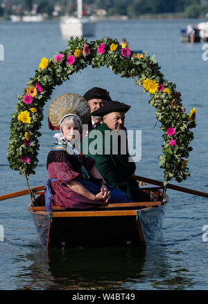 Radolfzell, Deutschland. 22. Juli, 2019. Träger von traditionellen Kostümen auf einem Boot mit Kränze mit Blumen geschmückt in den Hafen von Radolfzell am Bodensee während der Moos wasser Prozession. Die Prozession wurde in 1926 das erste Mal auf dem Wasser über den Bodensee. Es geht zurück bis in das 18. Jahrhundert. 1796 Die Bürger von Moos eine rinderseuche - aus Dankbarkeit für diese verschont blieben, die Veranstaltung findet jedes Jahr am dritten Montag im Juli. Quelle: Patrick Seeger/dpa/Alamy leben Nachrichten Stockfoto