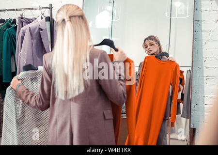 Blonde Frau mit langen, glatten Haaren auf der Suche nach Kleid Stockfoto