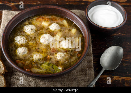 Hausgemachte Suppe mit Fleischbällchen in einem Ton Platte auf einem braunen Holz- Hintergrund. Neben der Platte ist ein Löffel und Salz Stockfoto