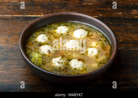 Hausgemachte Suppe mit Fleischbällchen in einem Ton Platte auf einem braunen Holz- Hintergrund Stockfoto