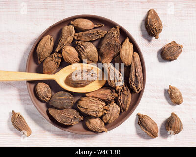 Schwarzer Cardamom (Amomum subulatum) auf einem braunen Ton Platte auf einem hölzernen Hintergrund mit Löffel Stockfoto