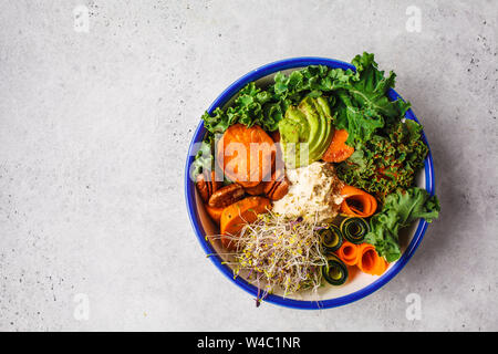 Gesund vegan Mittagessen in einer weißen Schüssel. Buddha Schüssel mit Avocados, süsse Kartoffeln, Rosenkohl und Gemüse. Stockfoto