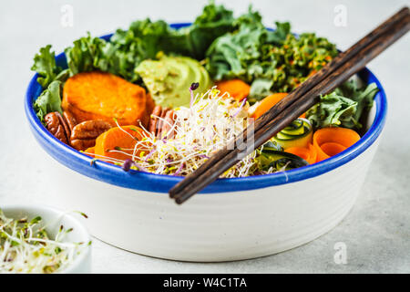 Gesund vegan Mittagessen in einer weißen Schüssel. Buddha Schüssel mit Avocados, süsse Kartoffeln, Rosenkohl und Gemüse. Stockfoto