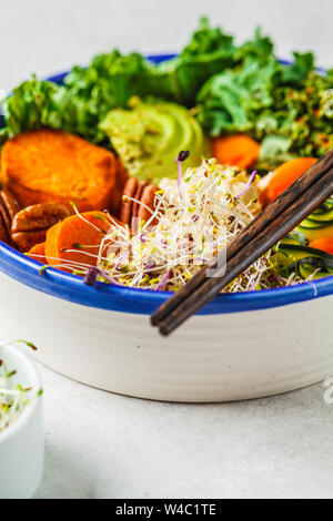 Gesund vegan Mittagessen in einer weißen Schüssel. Buddha Schüssel mit Avocados, süsse Kartoffeln, Rosenkohl und Gemüse. Stockfoto