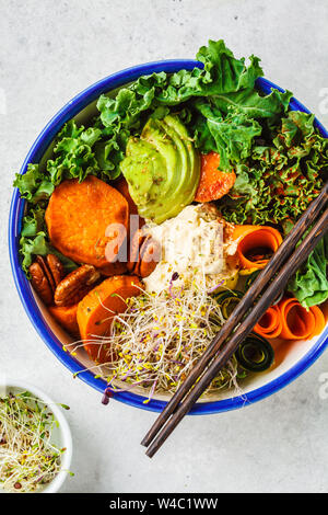 Gesund vegan Mittagessen in einer weißen Schüssel. Buddha Schüssel mit Avocados, süsse Kartoffeln, Rosenkohl und Gemüse. Stockfoto