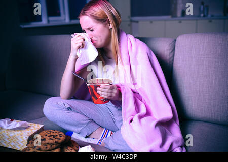 Junge Frau ansehen Film in der Nacht. Das Sitzen auf dem Sofa und weinte. Holding Gewebe in der Nähe des Kopfes. Eis essen. Sie traurigen Film oder TV-Serie Stockfoto