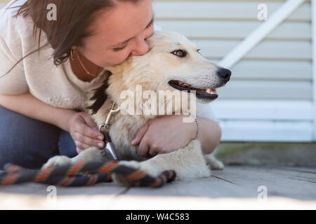 Foto von Frau umarmt einen weißen Hund in der Nähe von white Holzwand auf der Straße Stockfoto