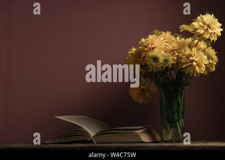 Alte Bücher und gelbe Blumen in Vase auf einem Holztisch aus Eiche, dunkel-rot Wand Hintergrund. Stockfoto