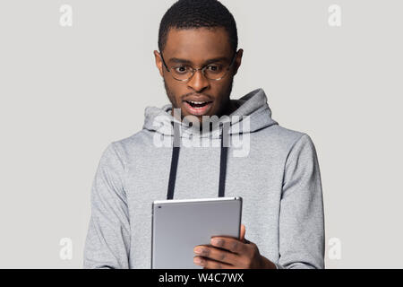 Überrascht schwarze männliche Blick auf Tablet durch unerwartete Nachrichten überrascht Stockfoto