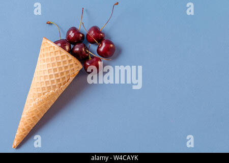 Flach frische Früchte, Kirsche in ein Waffeleisen Kegel auf blauem Hintergrund. Süßes Menü Konzept. Cope Platz für Ihren Text. Stockfoto