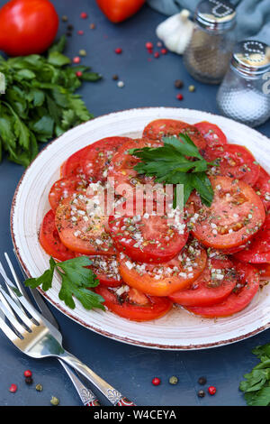 Vegetarische Vorspeise Tomaten mit Knoblauch, Petersilie, gekleidet mit Honig und Olivenöl in einer Platte auf einem dunklen Hintergrund entfernt, vertikale Foto, in der Nähe Stockfoto