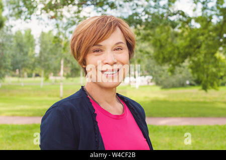 Closeup Portrait von gesunden Lächeln ältere Frau im Freien. Elegante reife rothaarige Frau mit kurzen Haaren lächelnd Stockfoto
