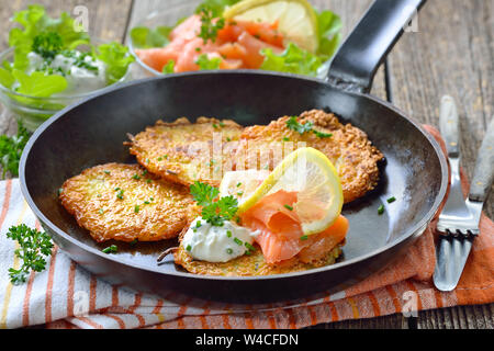 Knusprige Kartoffelpuffer mit Räucherlachs und saure Sahne mit frischen, grünen Kräutern in eine eiserne Pfanne serviert pan Stockfoto