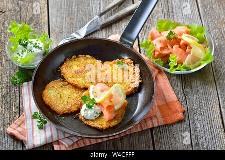 Knusprige Kartoffelpuffer mit Räucherlachs und saure Sahne mit frischen, grünen Kräutern in eine eiserne Pfanne serviert pan Stockfoto