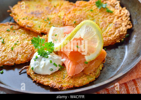 Knusprige Kartoffelpuffer mit Räucherlachs und saure Sahne mit frischen, grünen Kräutern in eine eiserne Pfanne serviert pan Stockfoto