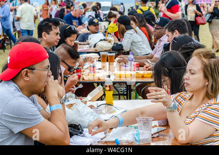 Die Leute sitzen Außen am Gestell Tisch und essen Essen gekauft Form geht im Barrio Fiesta in London. Stockfoto