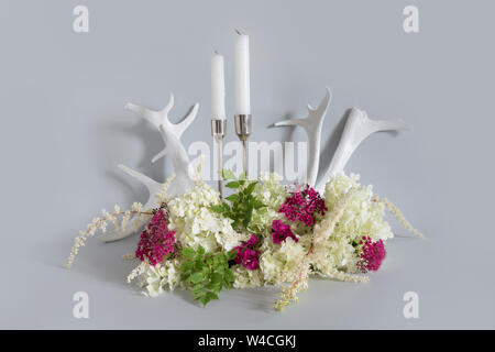 Weiß und Lila Wildblumen, Kerze und Rentier Geweih auf Pastell grau hinterlegt. Natur Zusammensetzung. Stockfoto