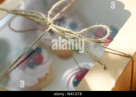 Weißes Feld mit einem Seil in ein Handwerk Paket vor dem Fenster gebunden. Berry cupcakes unter der transparenten Deckel sind bereit zu essen Stockfoto