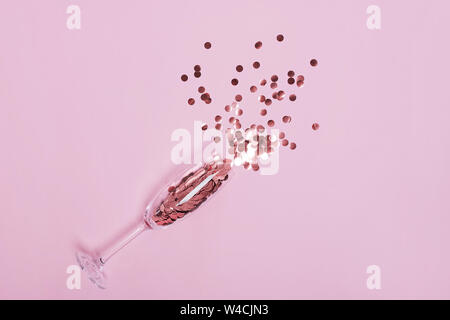 Kreis Rose Gold Konfetti in ein Champagnerglas auf rosa Hintergrund. Stockfoto