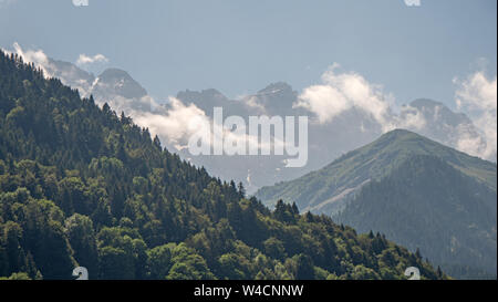 Luftbilder über eine Alpine Valley und üppig grüne Pinienwälder mit Chalets und hohen Berge, die das Tal. Stockfoto