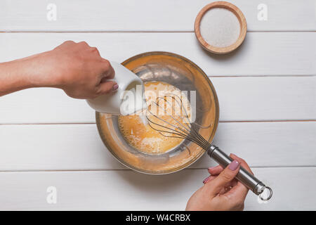 Die Frau Hände close-up mischen Eier und Zucker mit wisk in eine große Schüssel gießen und Milch oder Sahne. Stockfoto