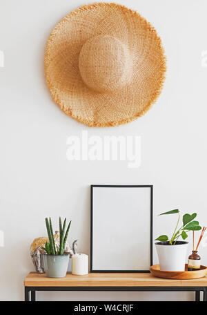 Modernes, minimalistisches Licht Interieur in Details. Straw Hat an der Wand über dem kleinen Holz- Konsole mit grünen Pflanzen Stockfoto