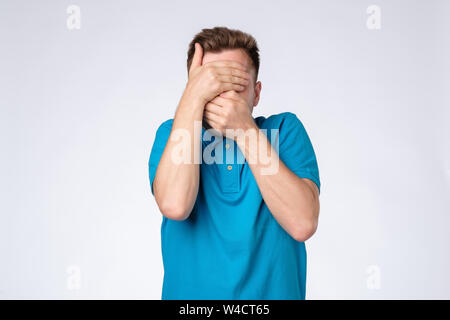 Jungen kaukasischen Mann im blauen Hemd schließt Gesicht mit den Händen versuchen, anonym zu bleiben. Stockfoto