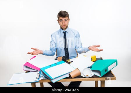 Der junge Mann hat eine komplette Verwirrung am Arbeitsplatz, er kann nicht organisieren seinen Platz und wichtige Dokumente finden. Konzept der Probleme im Büro, Business, Werbung, alltägliche Probleme. Stockfoto