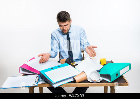 Der junge Mann hat eine komplette Verwirrung am Arbeitsplatz, er kann nicht organisieren seinen Platz und wichtige Dokumente finden. Konzept der Probleme im Büro, Business, Werbung, alltägliche Probleme. Stockfoto