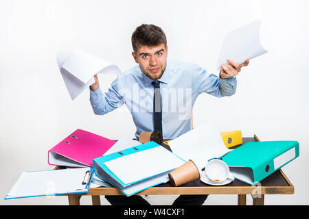 Der junge Mann hat eine komplette Verwirrung am Arbeitsplatz, er kann nicht organisieren seinen Platz und wichtige Dokumente finden. Konzept der Probleme im Büro, Business, Werbung, alltägliche Probleme. Stockfoto