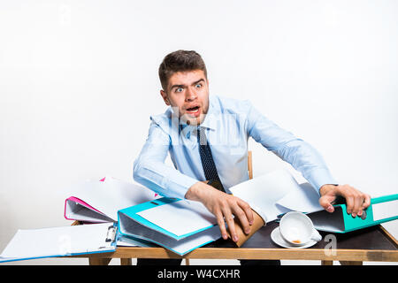 Der junge Mann hat eine komplette Verwirrung am Arbeitsplatz, er kann nicht organisieren seinen Platz und wichtige Dokumente finden. Konzept der Probleme im Büro, Business, Werbung, alltägliche Probleme. Stockfoto