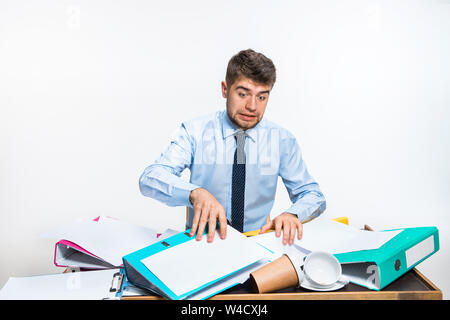 Der junge Mann hat eine komplette Verwirrung am Arbeitsplatz, er kann nicht organisieren seinen Platz und wichtige Dokumente finden. Konzept der Probleme im Büro, Business, Werbung, alltägliche Probleme. Stockfoto
