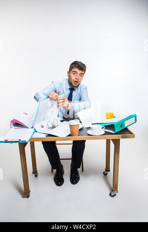 Der junge Mann hat eine komplette Verwirrung am Arbeitsplatz, er kann nicht organisieren seinen Platz und wichtige Dokumente finden. Konzept der Probleme im Büro, Business, Werbung, alltägliche Probleme. Stockfoto