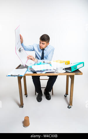 Der junge Mann hat eine komplette Verwirrung am Arbeitsplatz, er kann nicht organisieren seinen Platz und wichtige Dokumente finden. Konzept der Probleme im Büro, Business, Werbung, alltägliche Probleme. Stockfoto