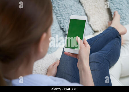 Blick über die Schulter der Frau liegt auf einem Sofa mit Green Screen Handy zu Hause Stockfoto