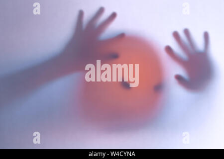 Halloween verschwommenen Hintergrund. Ein Geist wie ein Kürbis in Farbe hinter Glas. Schrecklich und schrecklichen Alptraum. Er klopft an, um das Fenster Stockfoto