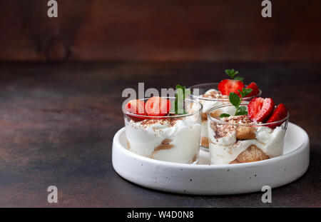 Tiramisu in ein Glas mit frischen Erdbeeren und Minze auf braunem Hintergrund Stockfoto
