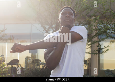 Portrait der afrikanischen amerikanischen Mann recken die Arme in der Stadt. Junge männliche fitness Kerl, warm bis in den Morgen Stockfoto
